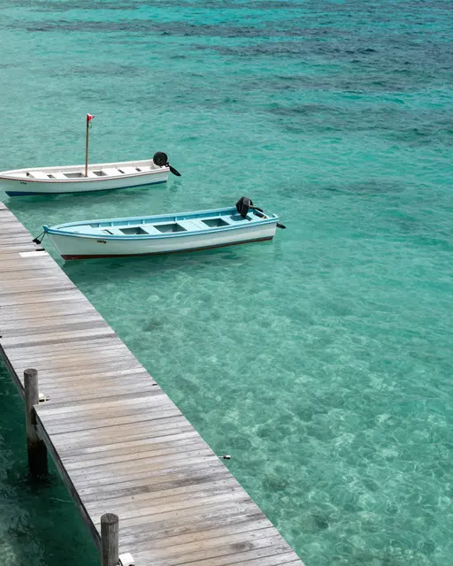 Weathered wooden jetty extends over clear turquoise water with two small moored motorboats
