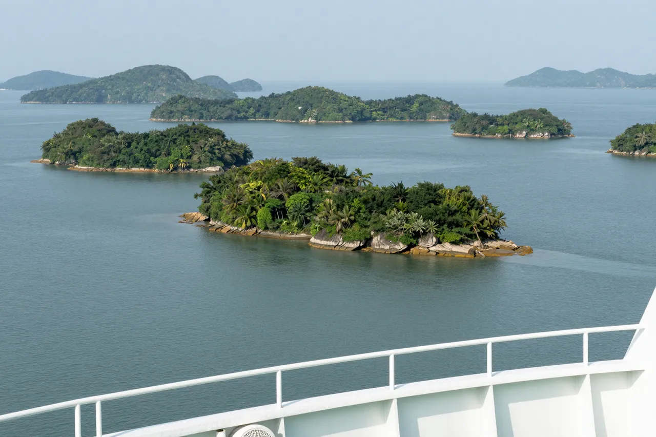 View from a ferry railing of lush green forested islands spread across calm blue water