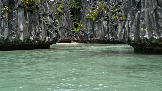 Turquoise clear lagoon water sits between tall jagged limestone cliffs dotted with tropical vegetation