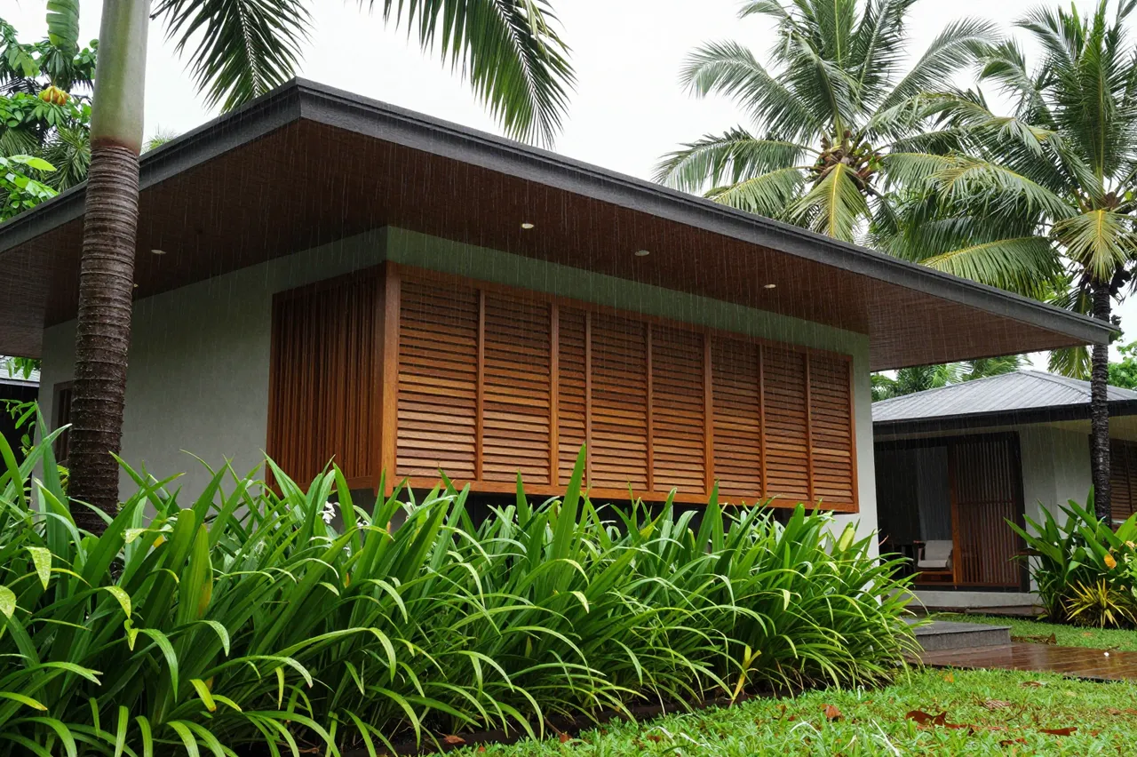 Modern tropical house with deep overhanging eaves and teak louvers surrounded by lush palms during light rain