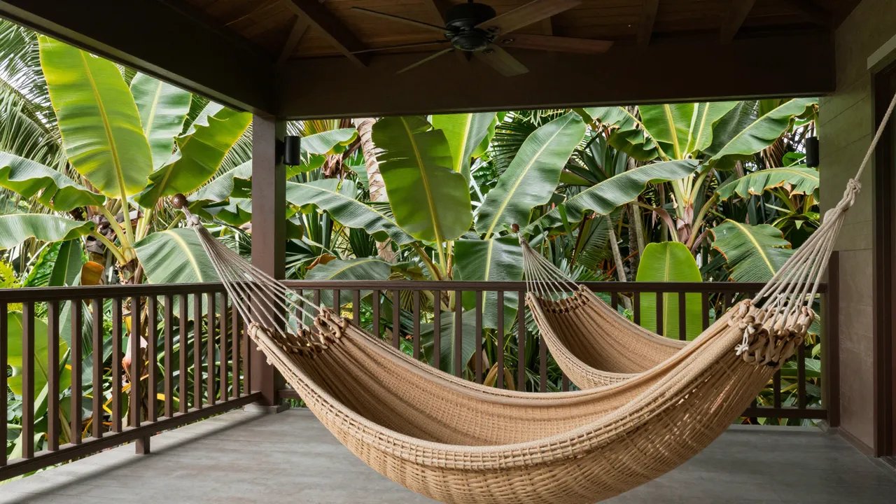 Covered tropical veranda with woven hammock chairs, overlooking lush banana plants outside the railing.