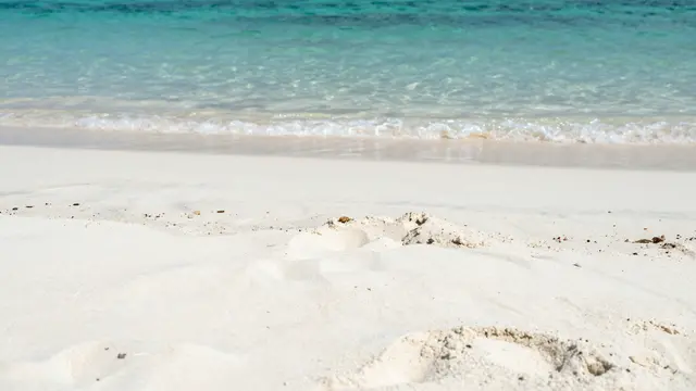 Gentle turquoise ocean waves lap onto bright white beach sand with plenty of empty copy space