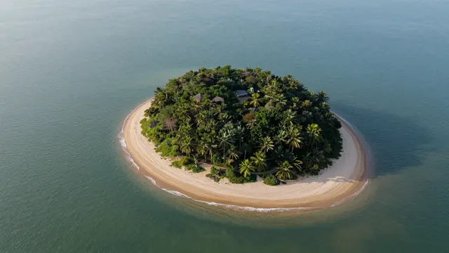 Aerial view of a small palm-covered tropical island ringed with sandy beach surrounded by calm turquoise sea.