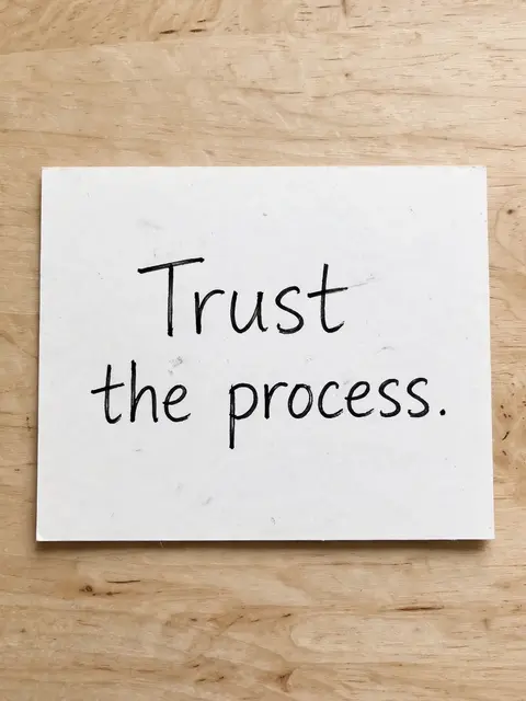 Handwritten "Trust the process." text in black ink on a white index card resting on a light wooden desk.