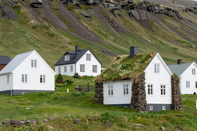 Traditional turf roofed and wooden houses sit on a lush green rocky Icelandic hillside