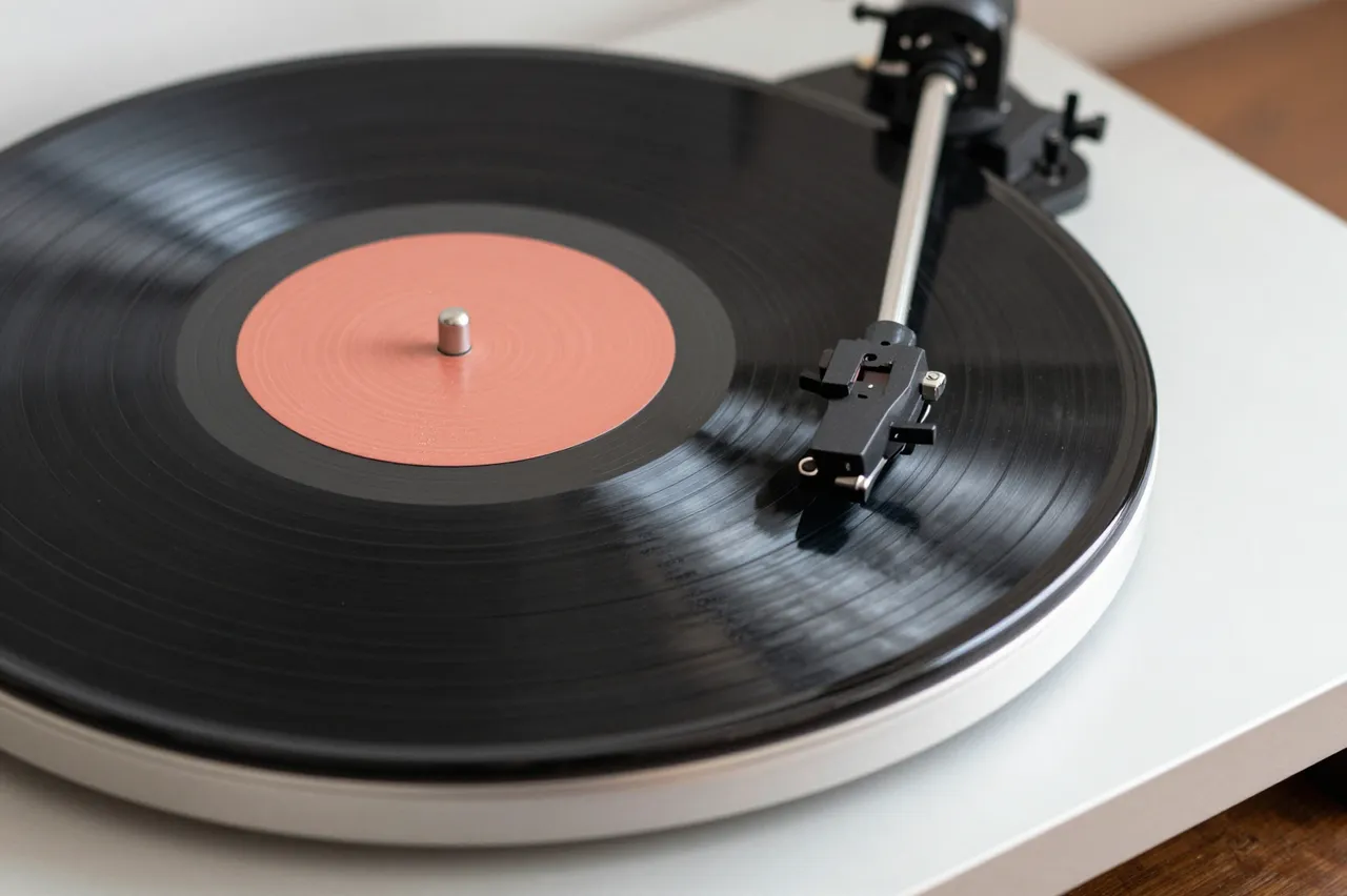 A close-up view of a vinyl record player with a black record and tonearm resting over the platter.