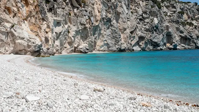 A quiet turquoise cove bordered by white pebbles and tall weathered limestone cliffs