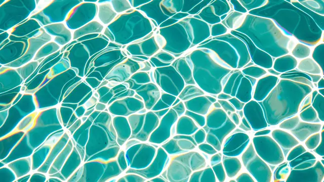 Shimmering wavy water caustics with iridescent rainbow fringes over bright turquoise pool water