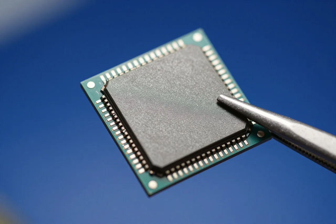 A macro close-up of a blank silicon chip held by metal tweezers against a soft blue background