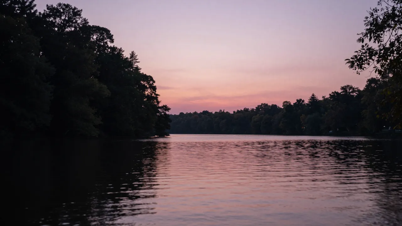 Pink and purple twilight sky reflects on calm lake water framed by dark silhouetted trees