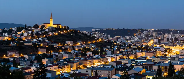Panoramic view of a lit hillside city with a prominent church spire at blue hour twilight