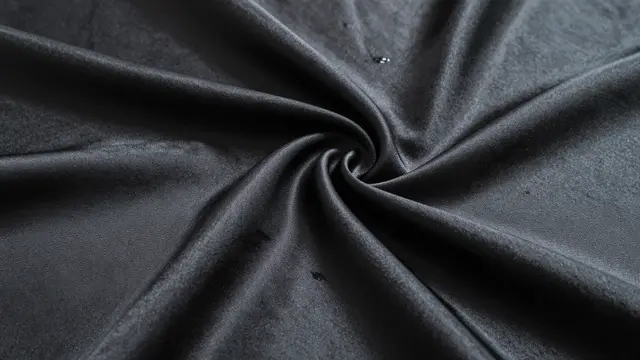 Close-up of twisted black satin fabric with soft rippling folds and subtle sheen