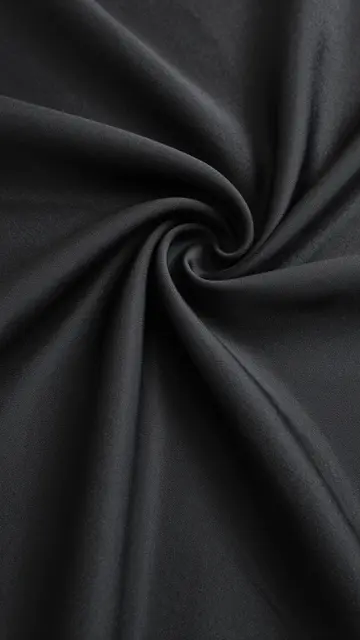 Close-up view of soft twisted black silk fabric with smooth curved folds spiraling to a center point