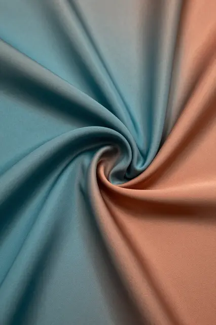 Full frame close-up of shot silk fabric twisted into a swirling spiral fold, shifting between teal and warm copper tones