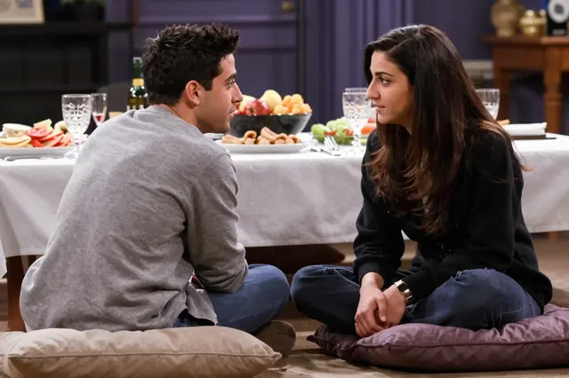 A mixed-race man and Middle Eastern woman sit cross-legged on floor cushions facing each other across a low table of festive