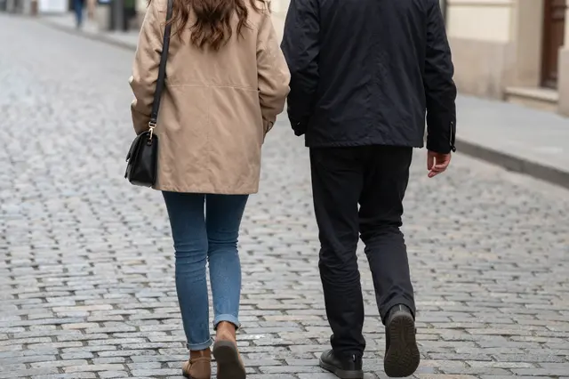 Back view of two people walking side by side along a cobblestone city street