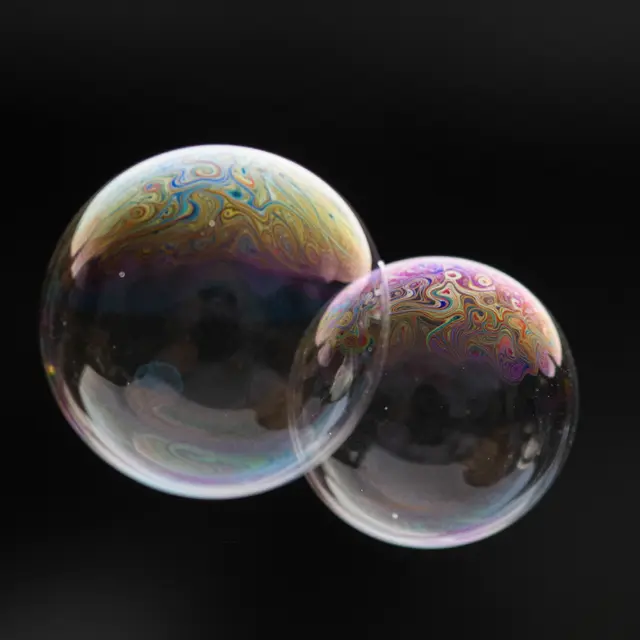 Two touching soap bubbles with swirling rainbow iridescent film against a solid black background