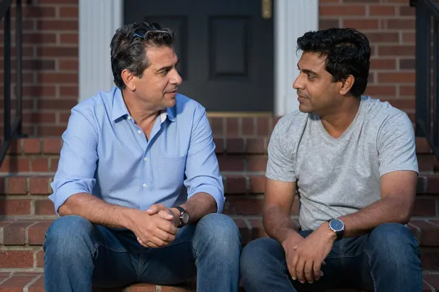 Two middle aged men sit together on brick home steps having a quiet conversation