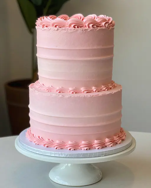Two tier pink ombre buttercream cake with ruffled piping on a white cake stand