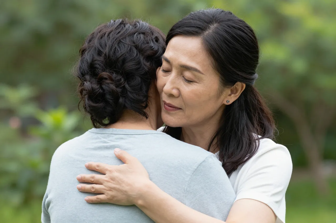 Two adult women share a warm embrace outdoors among green foliage