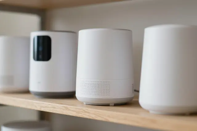 Row of minimal white unbranded smart home devices arranged on a light wooden shelf.