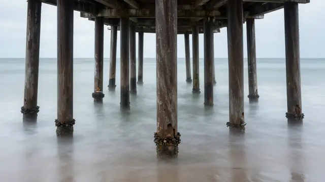 Weathered wooden pier pilings stand in smooth long-exposure misty ocean water