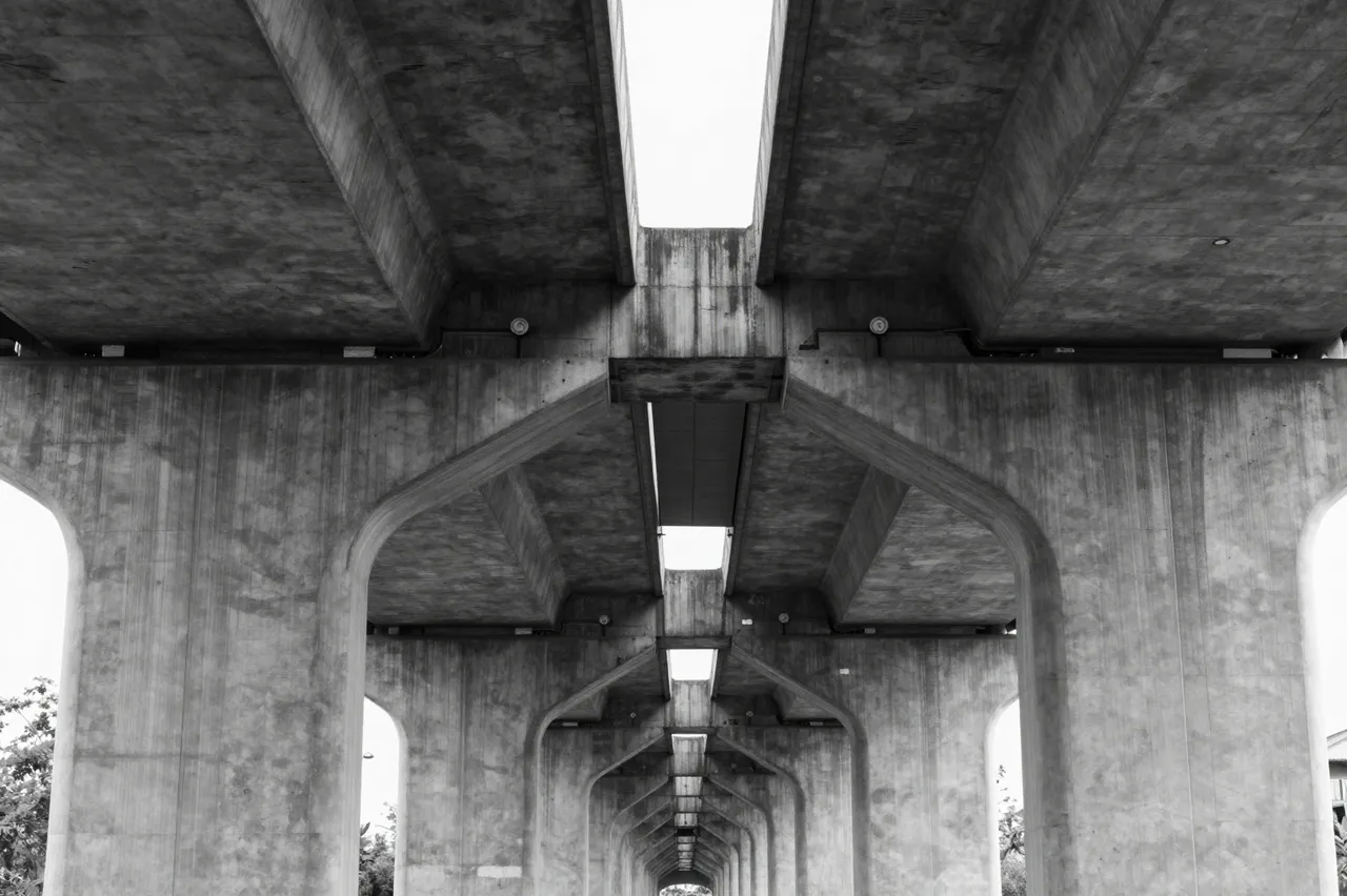 Low angle black and white view of repeating concrete overpass pillars receding into the distance