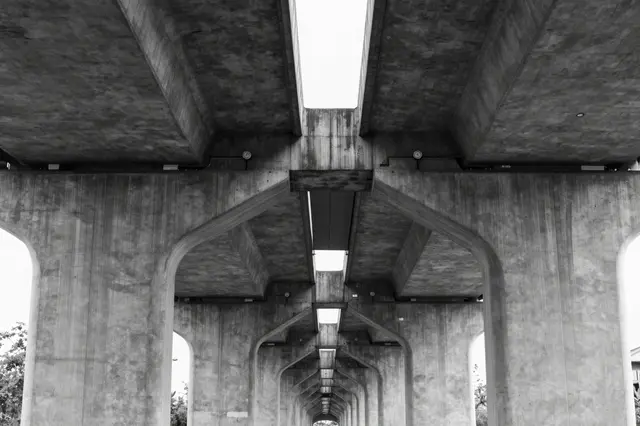 Low angle black and white view of repeating concrete overpass pillars receding into the distance