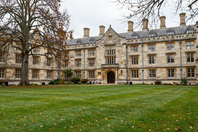 Grassy campus lawn stretches before an ornate old stone university building on an overcast autumn day