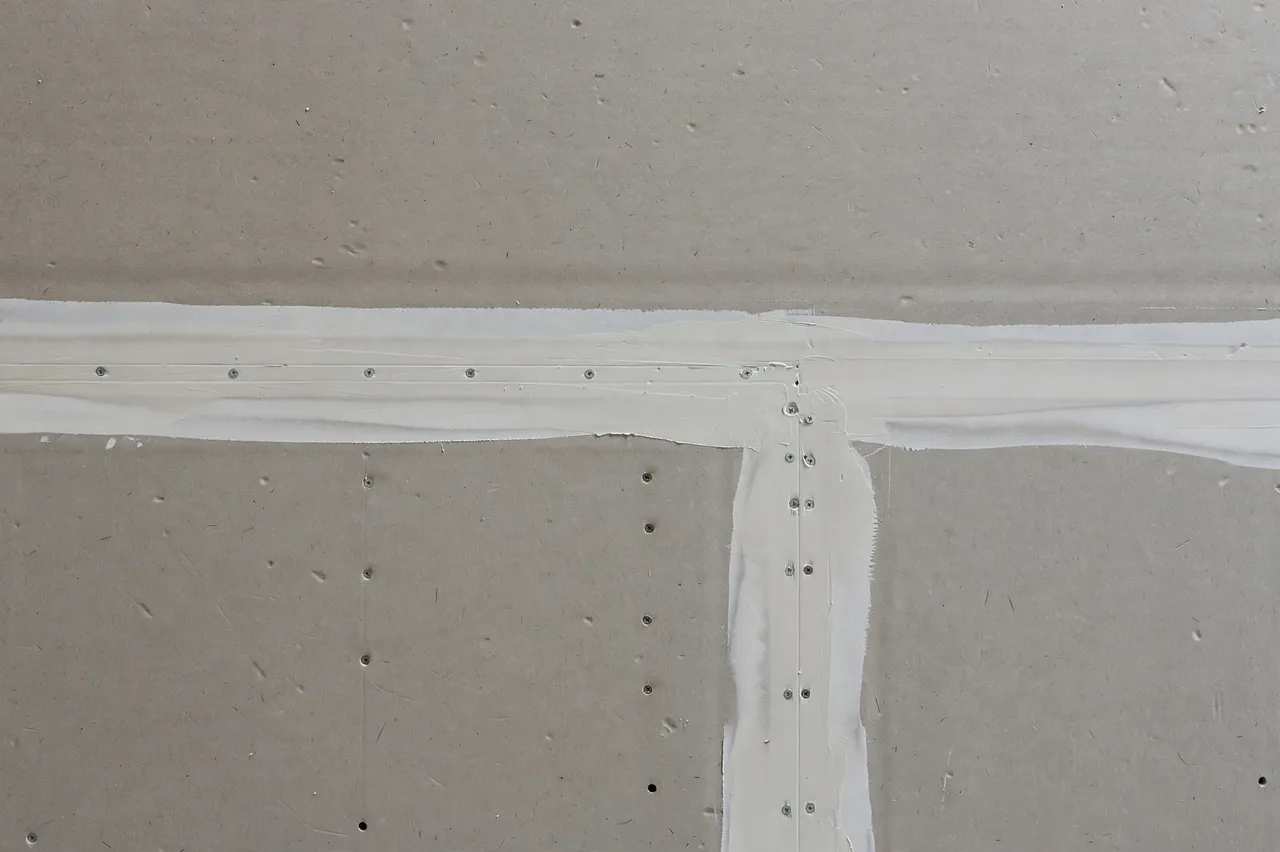 Full frame close-up of unfinished gray drywall with joint compound seams and visible screw spots under flat even light