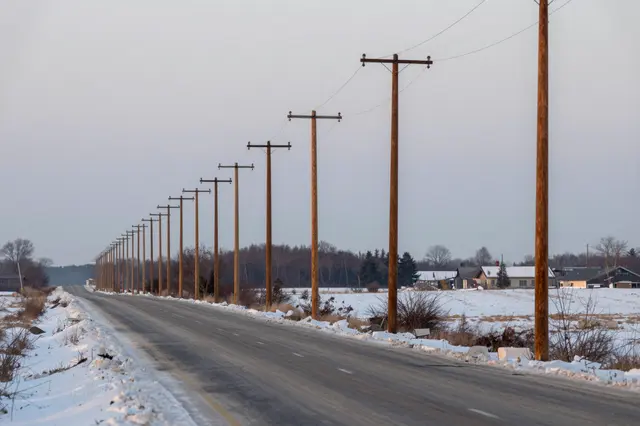 Row of wooden utility poles lines a snow-dusted empty country road at pale dusk