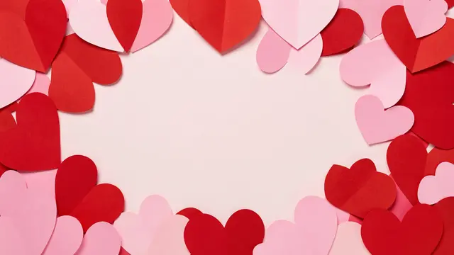 Frame of red and pink paper hearts surrounding a blank pale pink central copy space