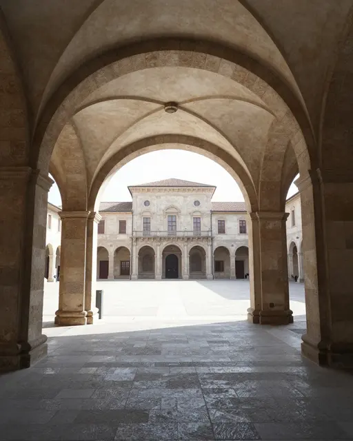 Stone vaulted covered passage frames a sunlit historic palace courtyard on a bright day