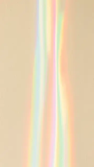 Soft vertical rainbow prismatic light bands stream down a textured cream wall