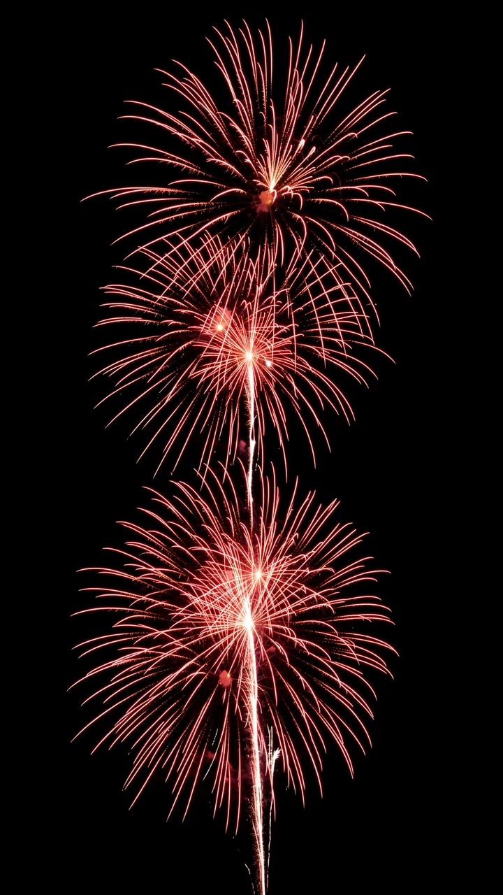 Stacked red and white firework bursts glow brightly against a solid pure black background