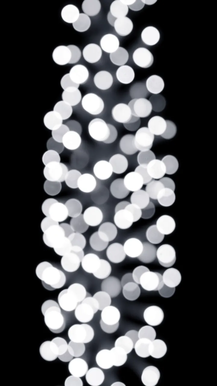 Vertical arrangement of soft white and gray blurred bokeh lights on a solid pure black background