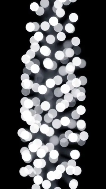 Vertical arrangement of soft white and gray blurred bokeh lights on a solid pure black background