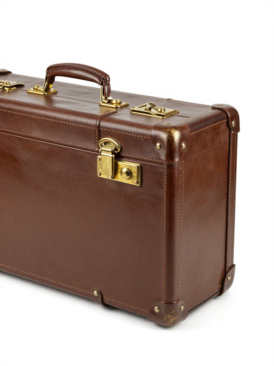 A side-angle view of a vintage brown leather suitcase with brass hardware on a plain white studio background