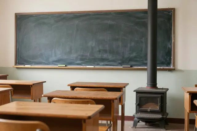 Empty old one-room school interior with wooden desks, cast iron stove, and blank chalkboard