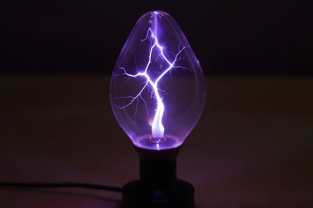 A plasma lamp with branching violet lightning filaments glows against a dark blurred background.