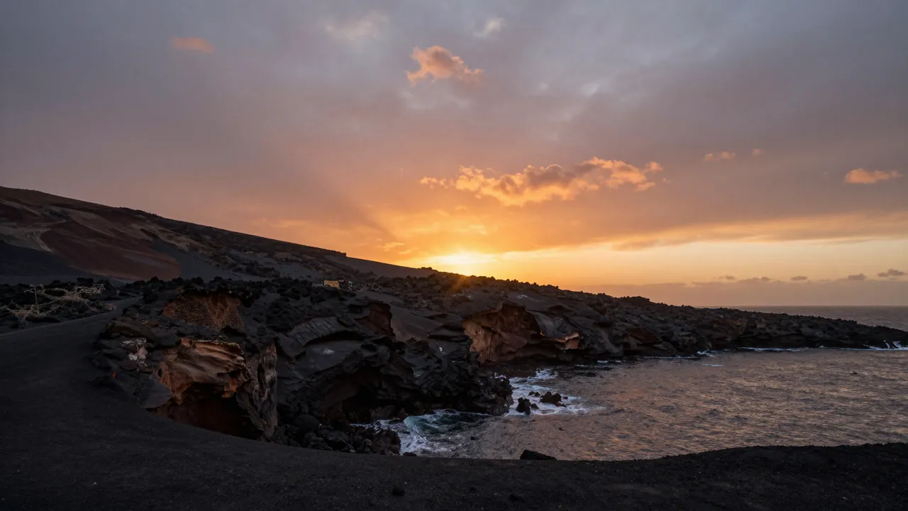 Blazing orange sunset glows over jagged black volcanic rock along a coastal ocean shore