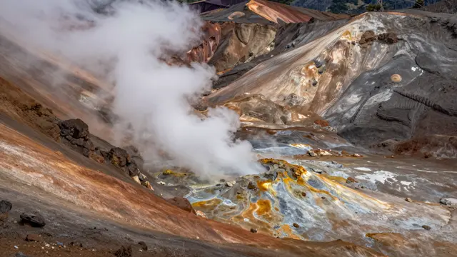 Steam rises from a fumarole across colorful mineral-stained volcanic mountain slopes
