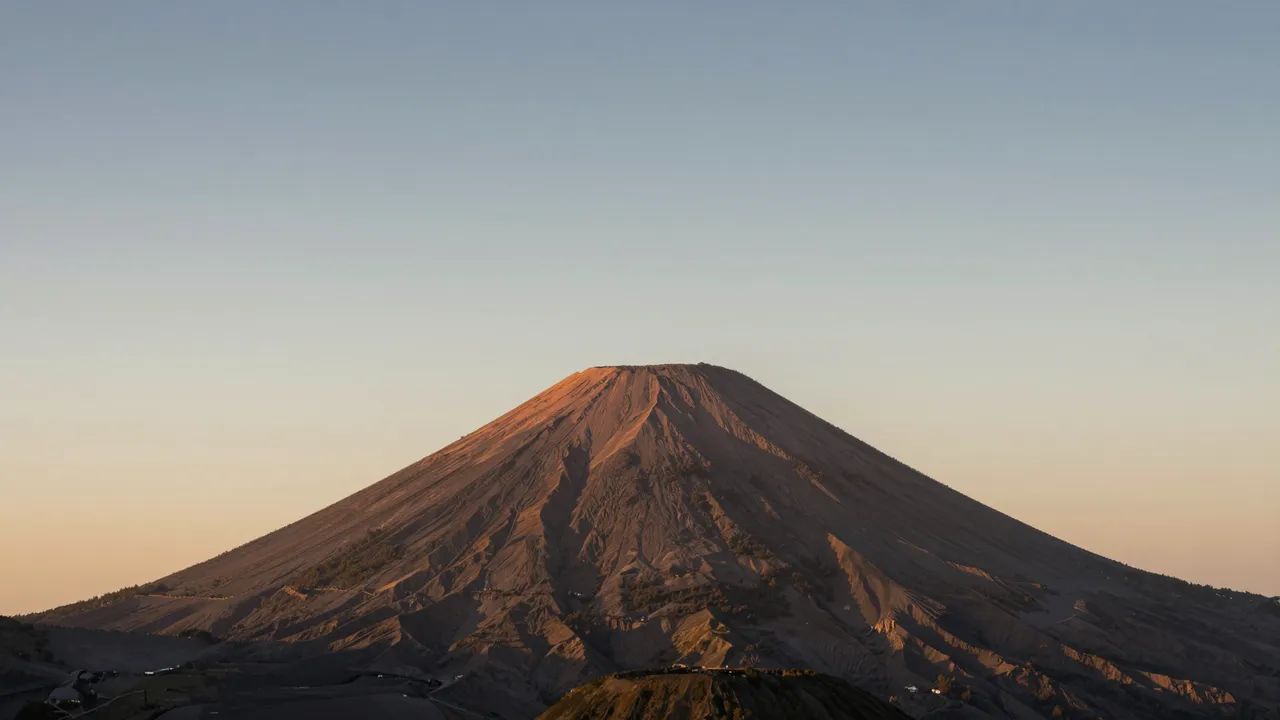 A conical volcano is lit by warm golden sunset light beneath a soft gradient sky
