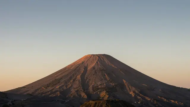 A conical volcano is lit by warm golden sunset light beneath a soft gradient sky