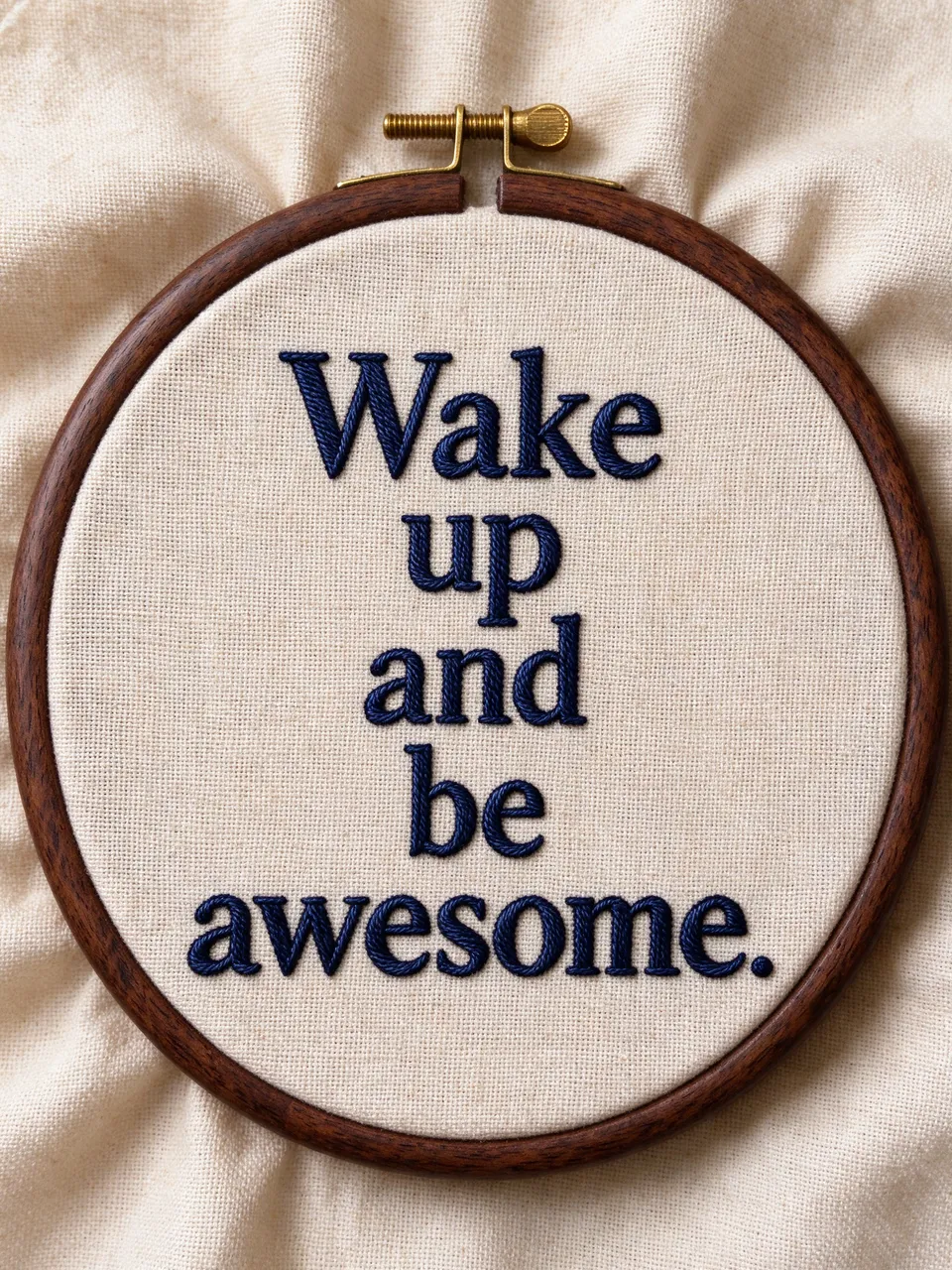Navy embroidered text "Wake up and be awesome." stitched on natural linen in a wooden embroidery hoop
