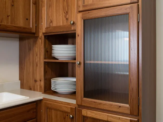 Detail of walnut wood butler's pantry cabinetry with stacked white plates, fluted glass door and small sink