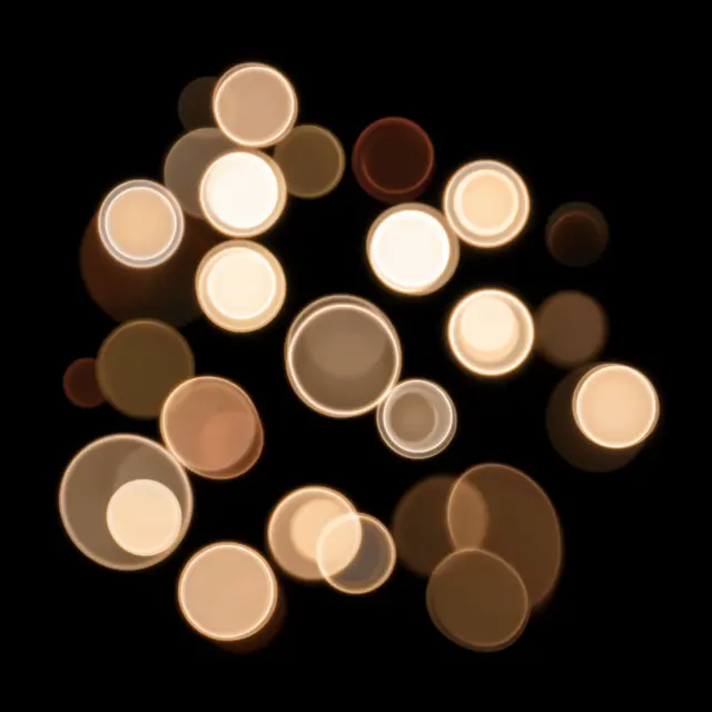 Glowing warm toned bokeh circles with bright rims float against a solid pure black background