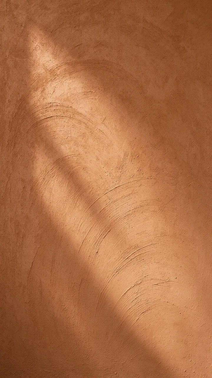 Smooth warm brown earthen clay plaster wall with soft trowel sweeps and side lighting