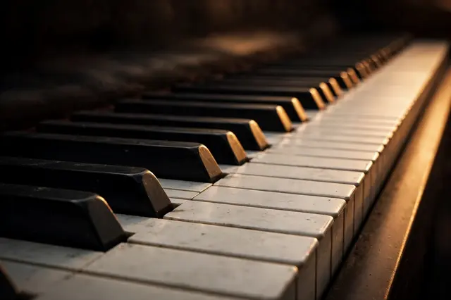 Low angle close-up of piano keys lit by warm fading lamplight falling into dark shadow