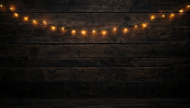 A strand of glowing warm fairy lights strung across a dark horizontal wooden plank wall with empty space below.
